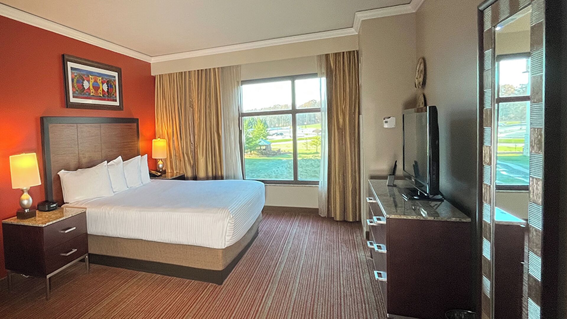 Habitación de hotel con una cama grande, televisión, escritorio con lámpara y ventana con cortinas.