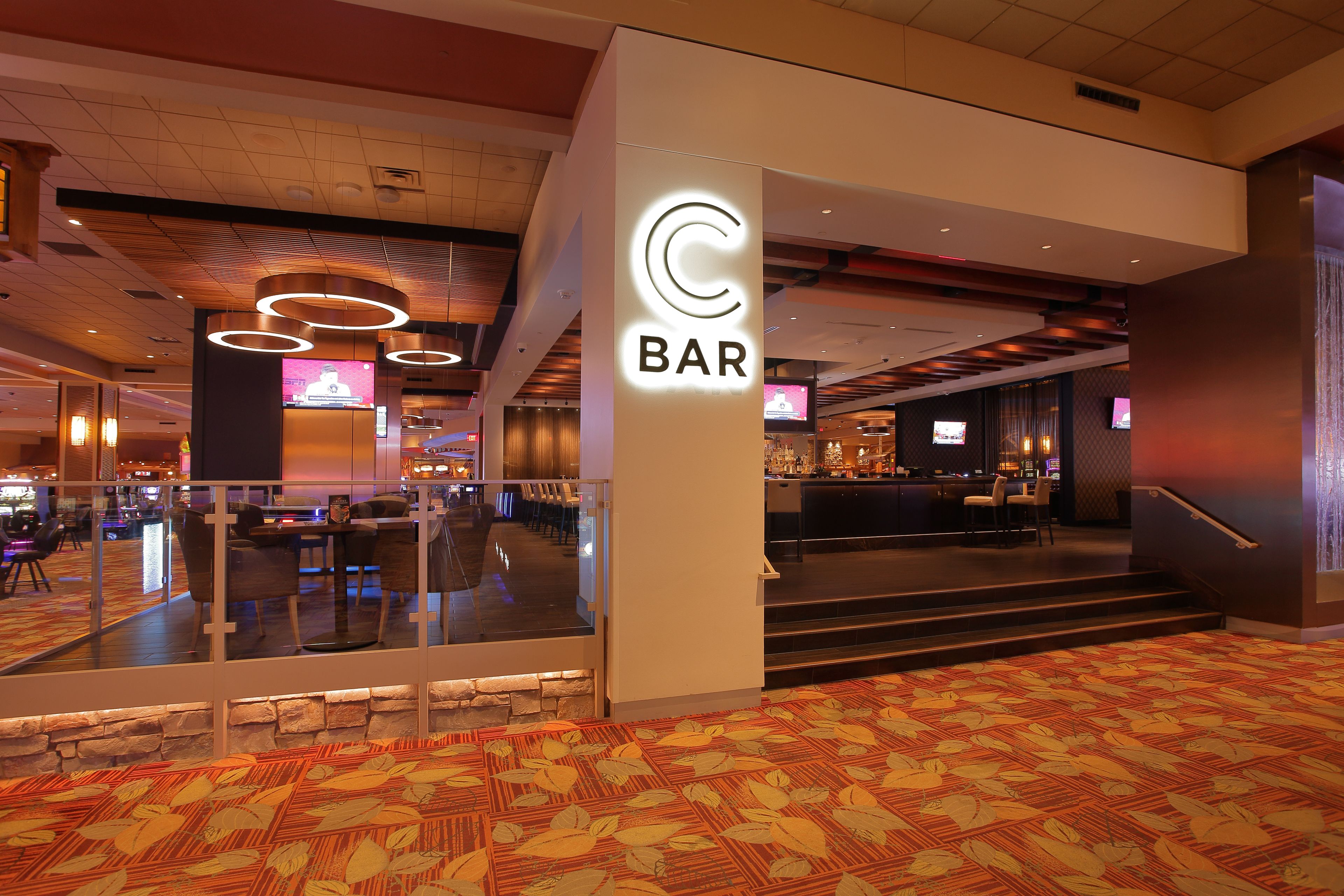 Un hall de hotel con zona de bar, barandas de cristal y alfombra estampada.
