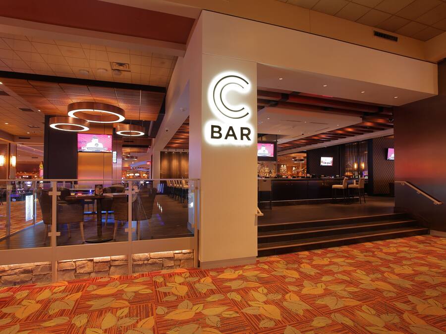 Un hall de hotel con zona de bar, barandas de cristal y alfombra estampada.