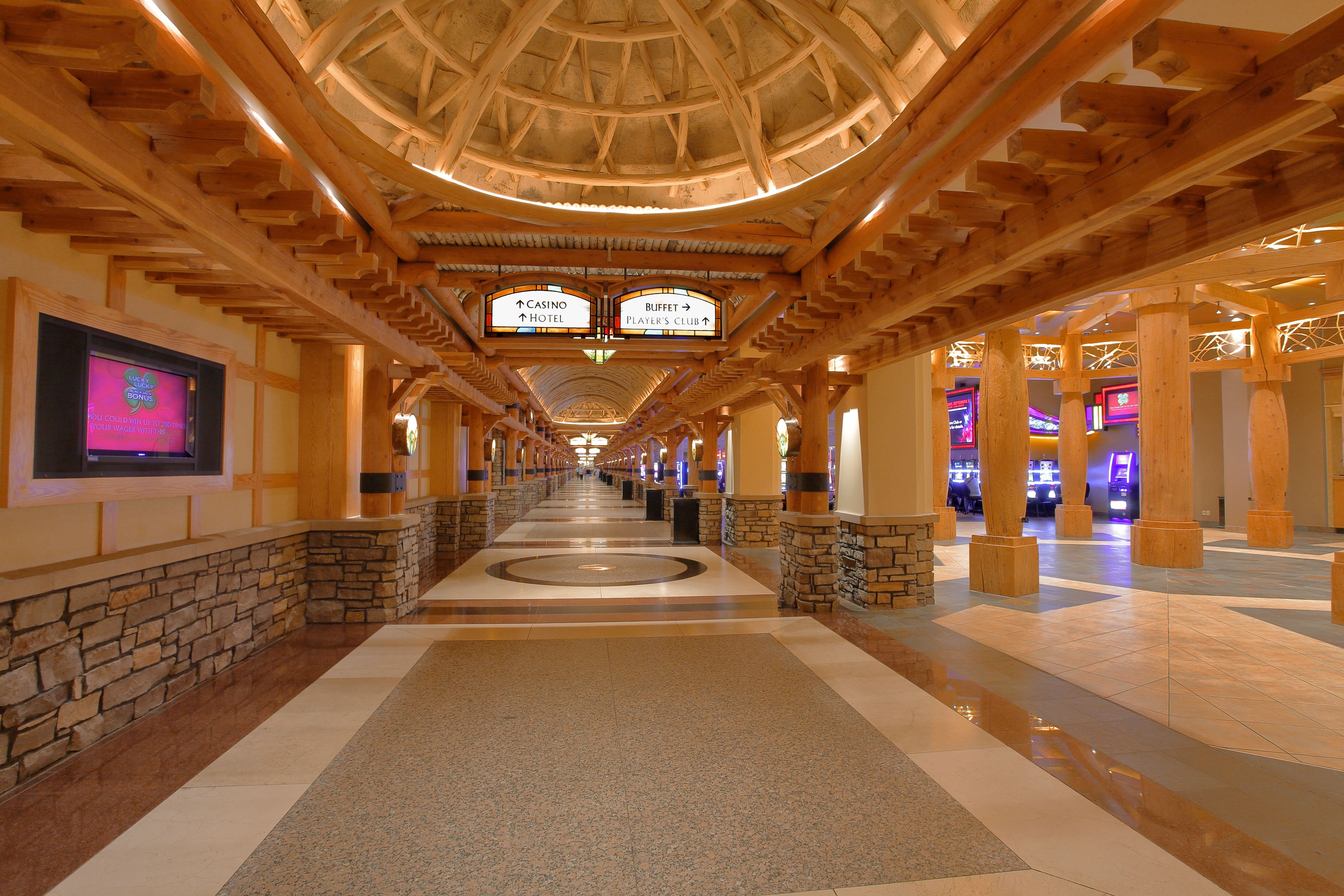 A hotel corridor with a wooden ceiling, stone walls, and directional signs to the casino, hotel, and player's club.