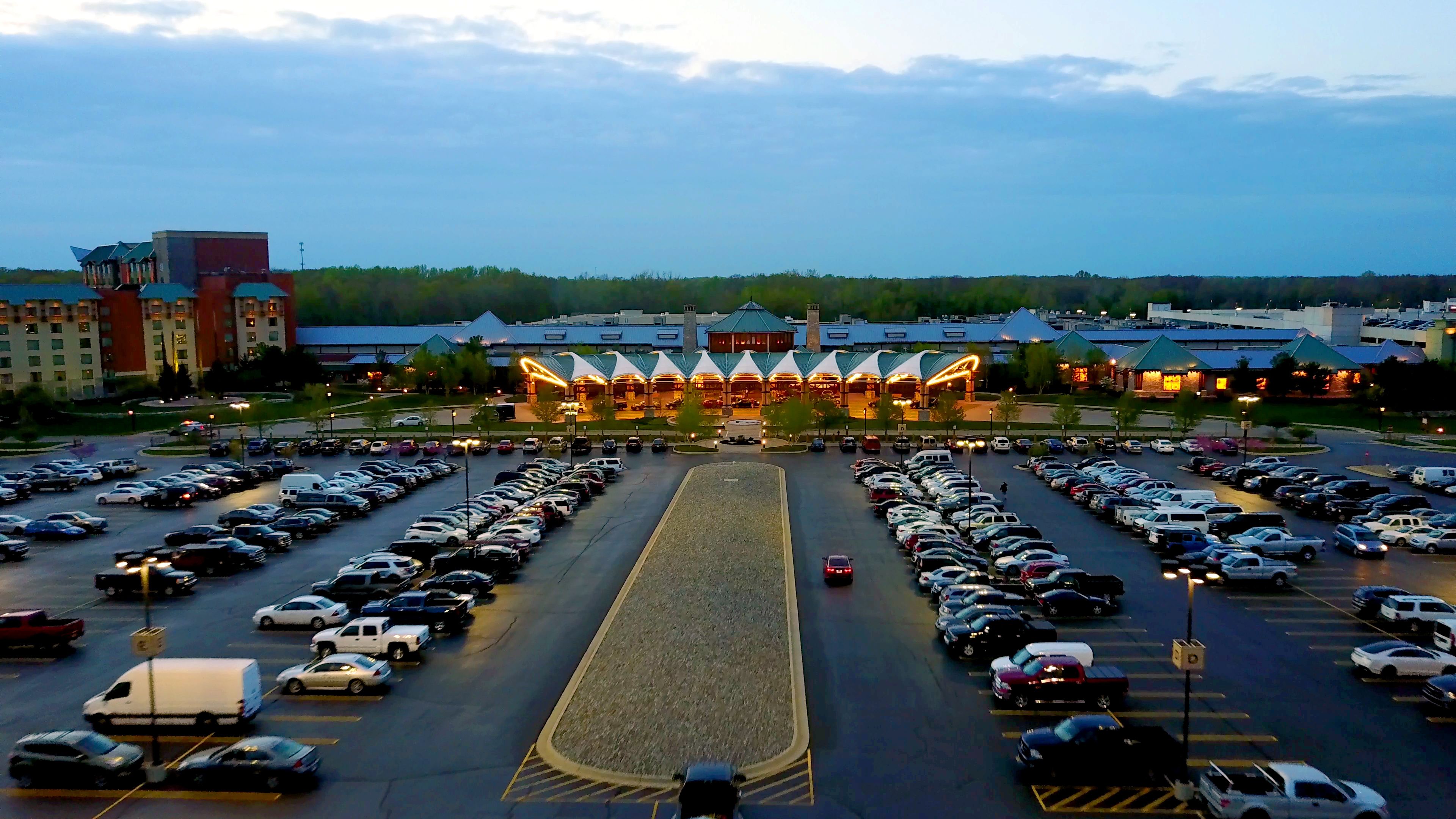 A large parking lot with multiple rows of cars and a building with a distinctive roof in the background.