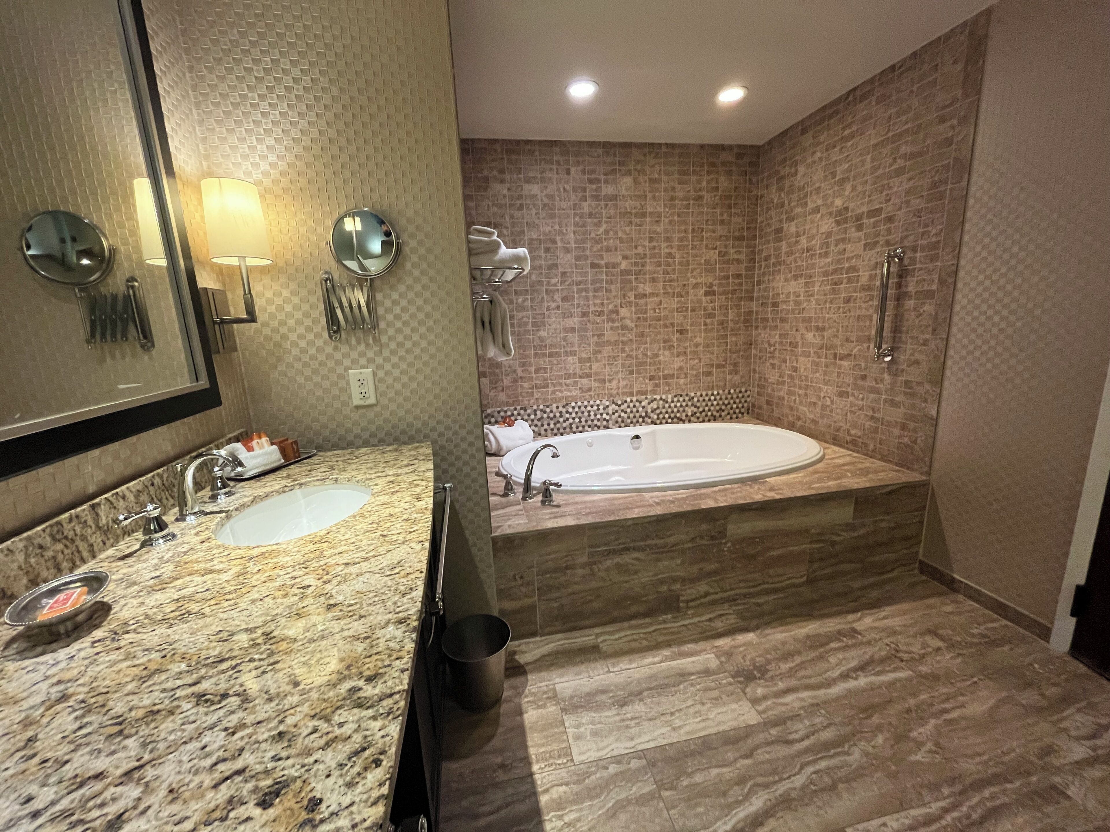 A modern bathroom with two sinks, a large bathtub, and a mirror with lights.