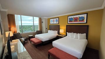 Quarto de hotel com duas camas, uma escrivaninha, uma cadeira, uma mesinha e vista para o exterior.