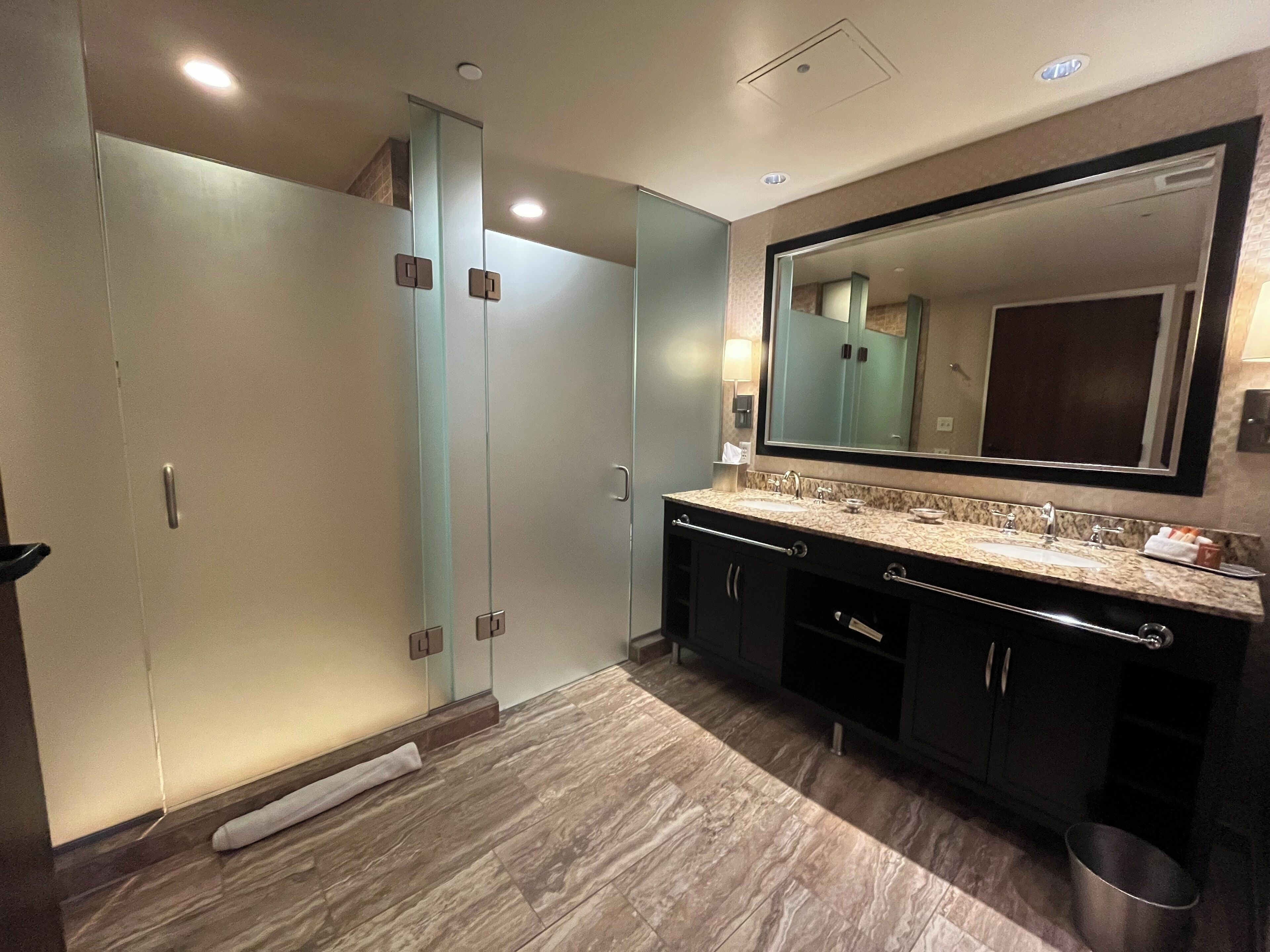 Un baño moderno con ducha de vidrio, un espejo grande y encimera de mármol.
