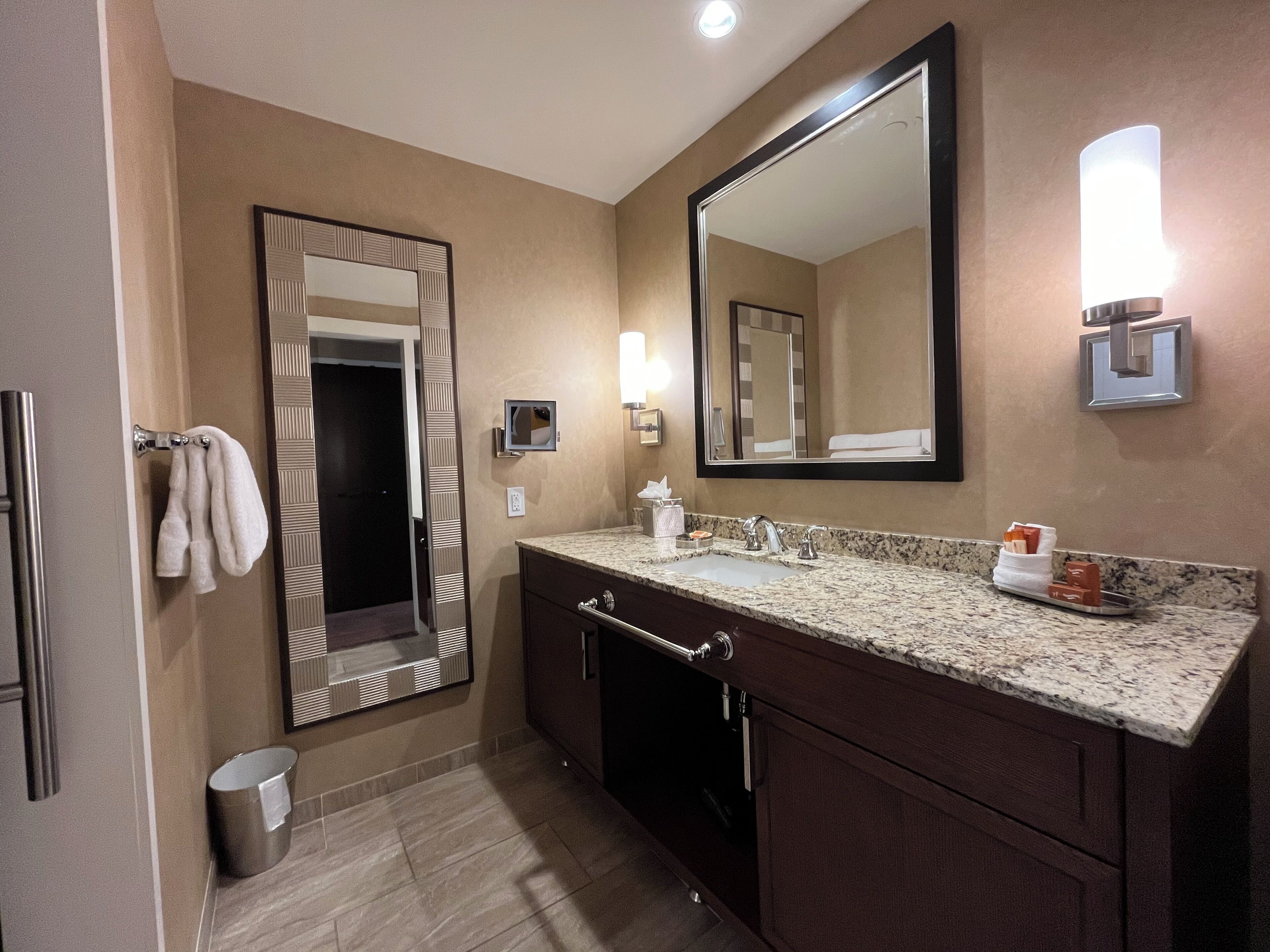 Ein Badezimmer mit Waschbecken, Spiegel, Handtuchhalter und Mülleimer.