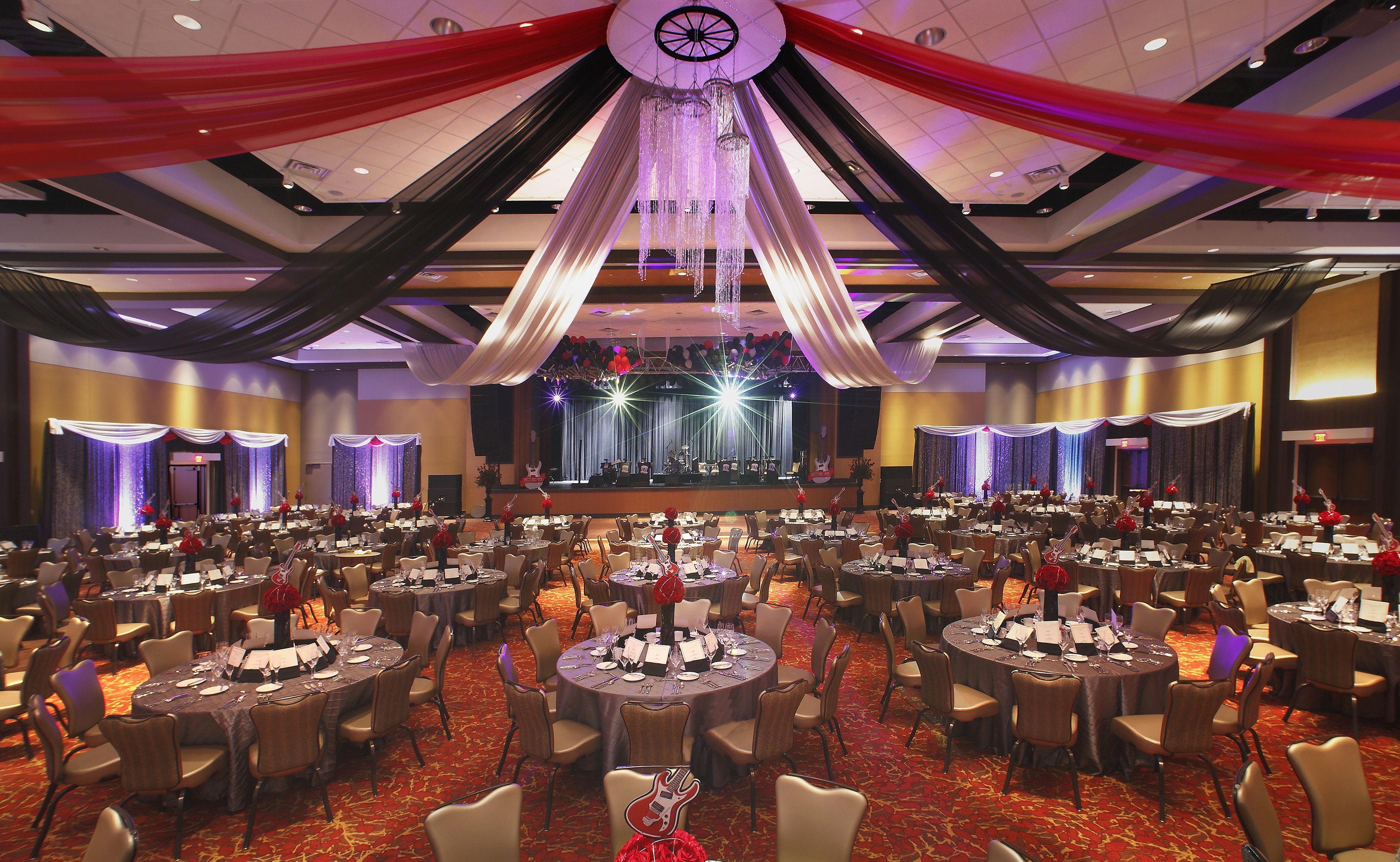A large banquet hall with round tables, a stage with musical instruments, and draped curtains.