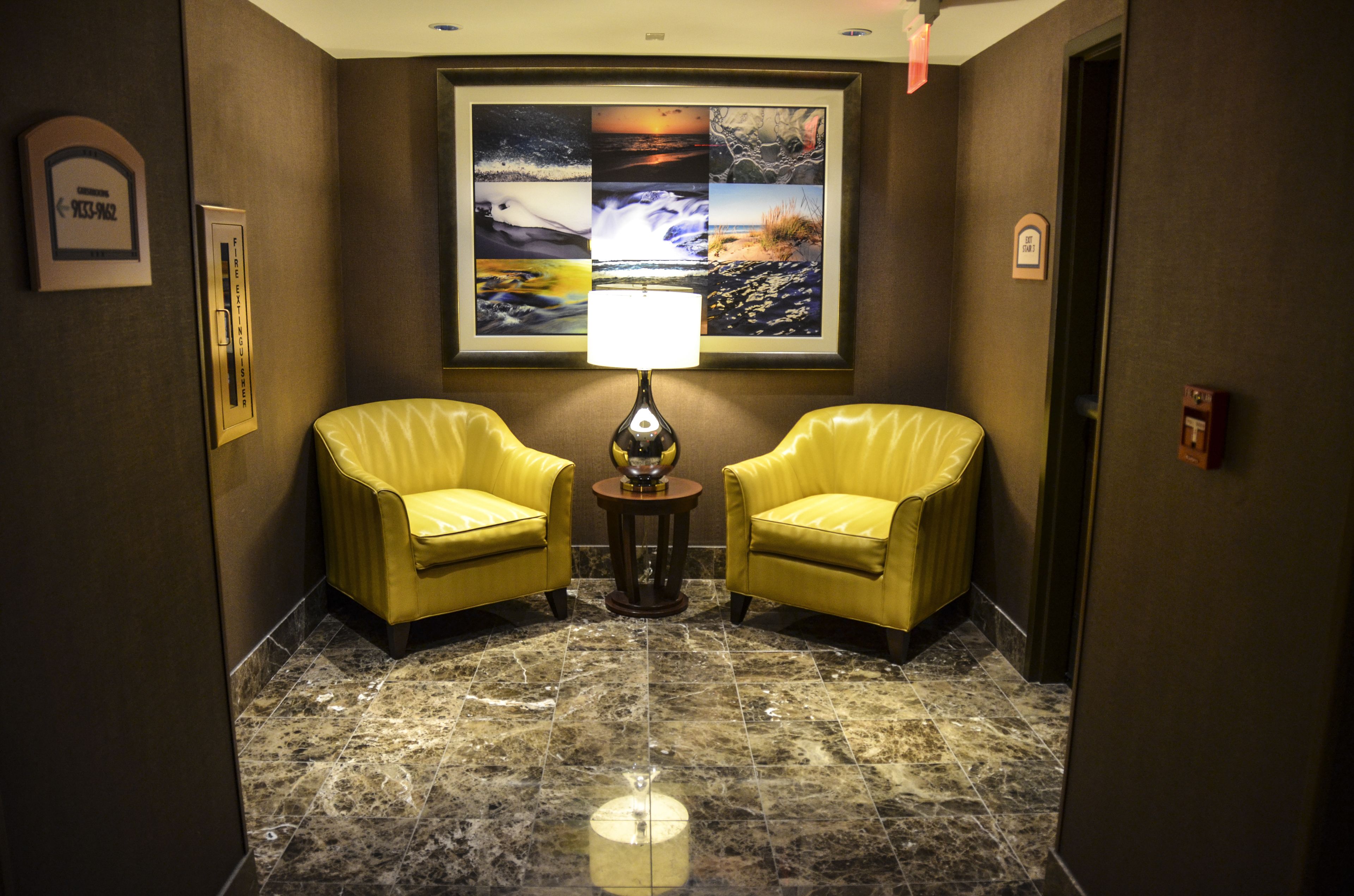 A lobby with two yellow armchairs, a marble floor, and a wall-mounted lamp.