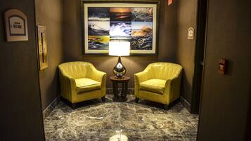 A lobby with two yellow armchairs, a marble floor, and a wall-mounted lamp.