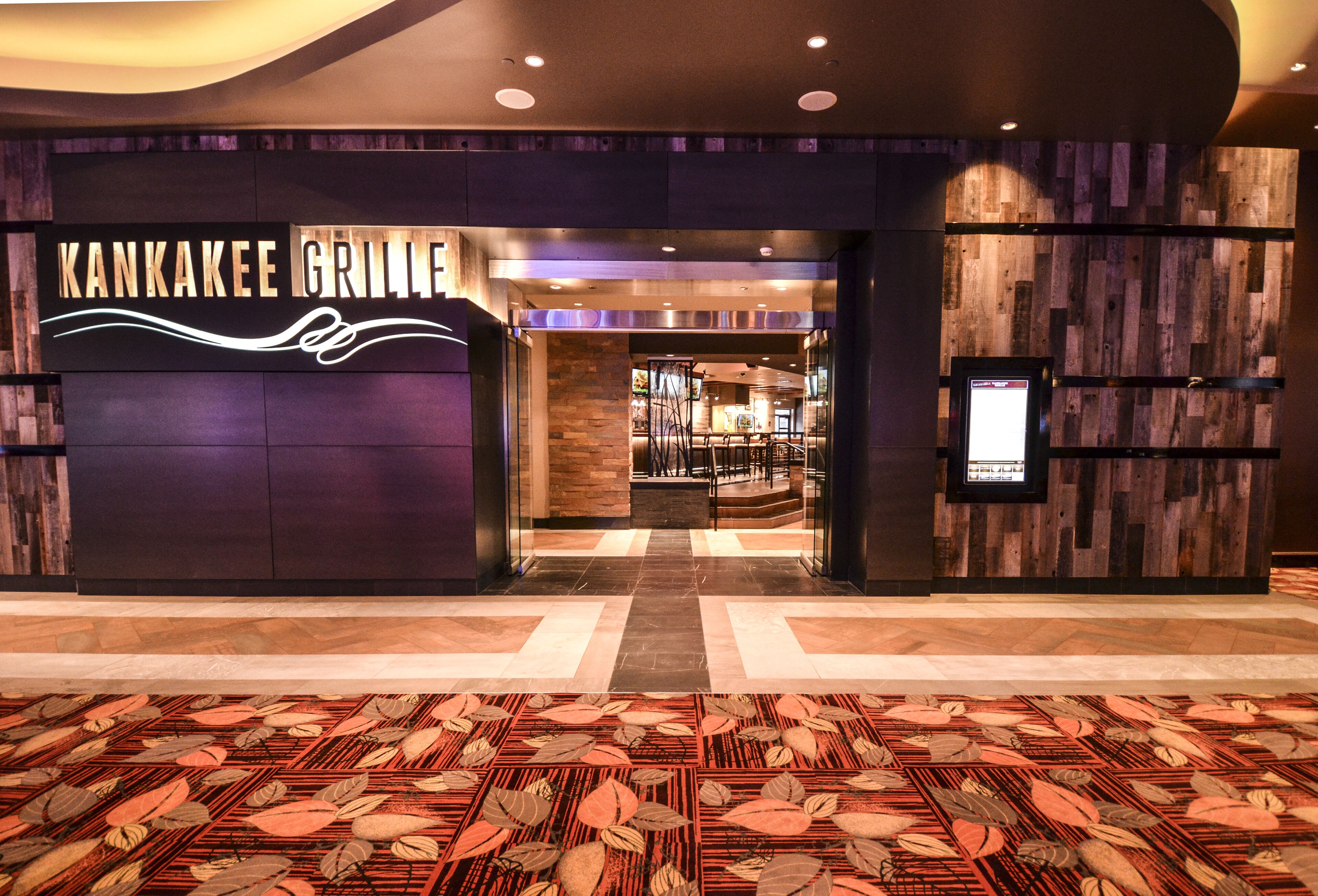 A modern entrance to Kankakee Grille with a checkered floor pattern and a wooden wall backdrop.