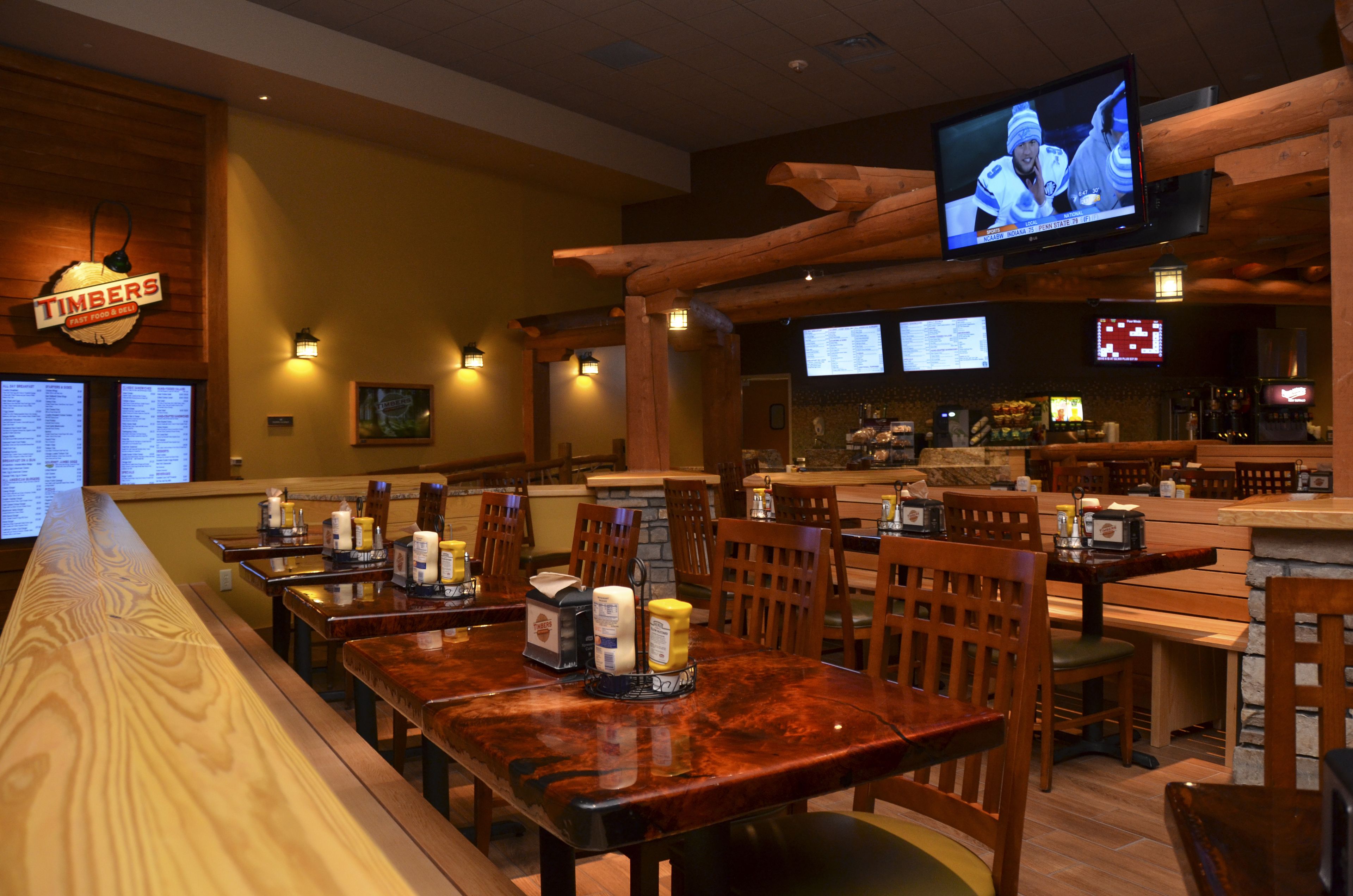 Un restaurante con mesas y sillas de madera, una zona de bar y una pantalla de televisión mostrando un partido de hockey.