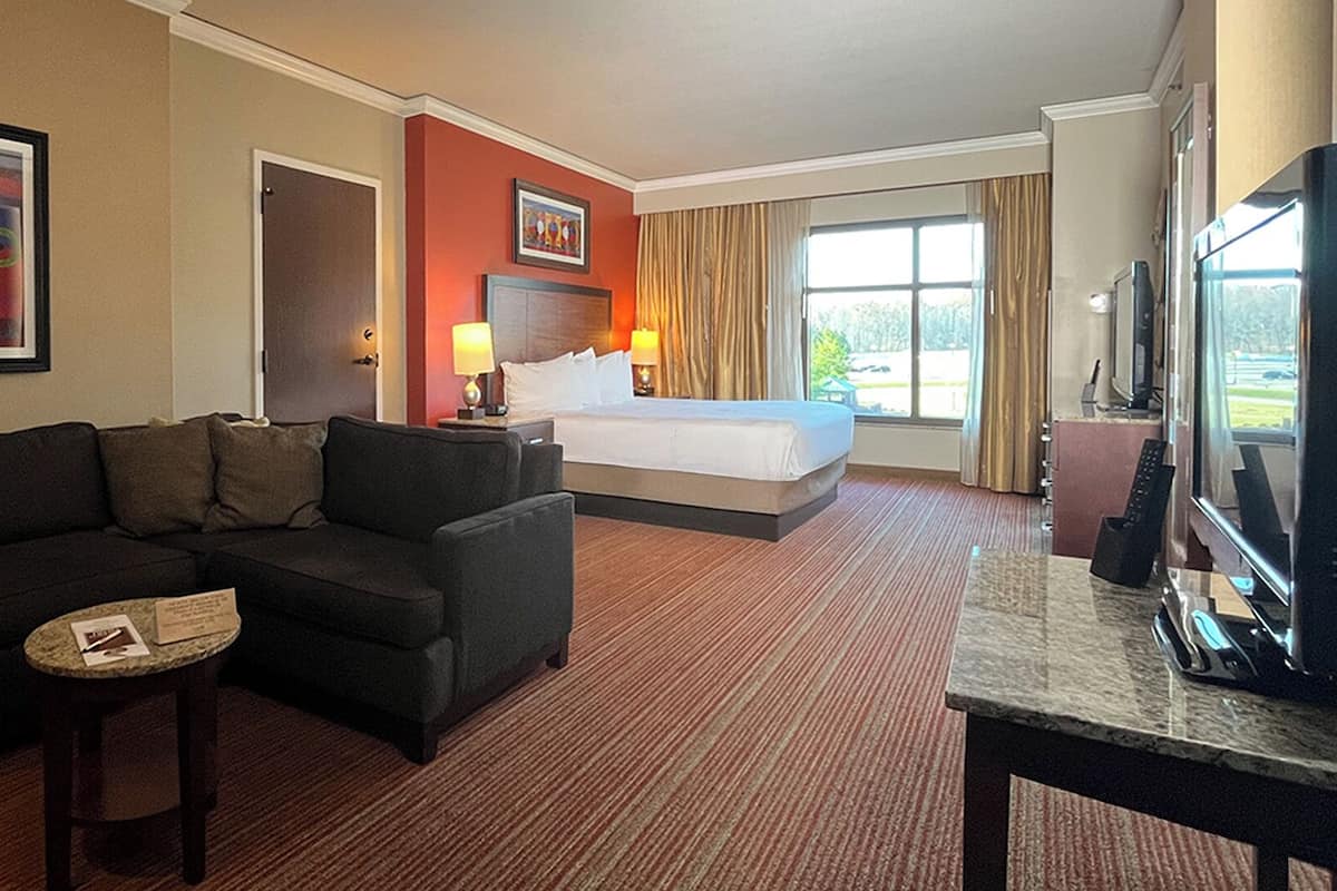 Ein Hotelzimmer mit Bett, einer Couch, einem kleinen Tisch, einem Fernseher und einem Fenster mit Vorhängen.