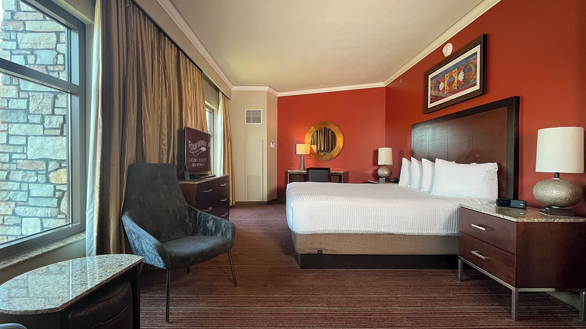 Habitación de hotel con una cama grande, una silla, un escritorio, una lámpara y un espejo montado en la pared.