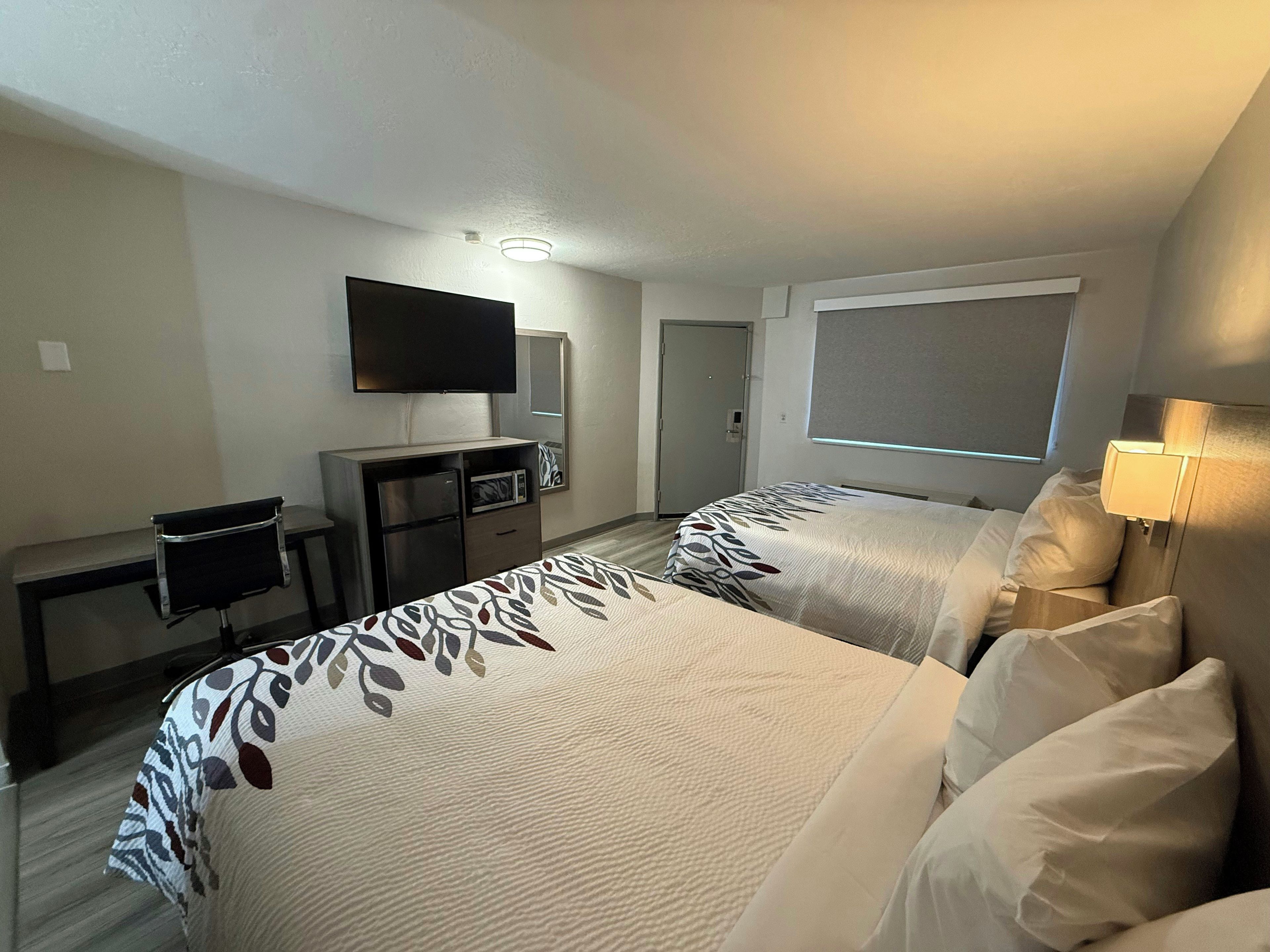 Habitación de hotel con dos camas, un escritorio con silla, televisión y ventana.