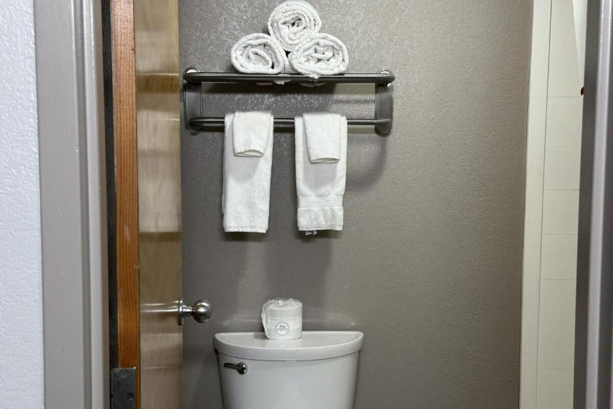 A bathroom with a toilet, a towel rack with rolled towels, and a toilet paper holder.