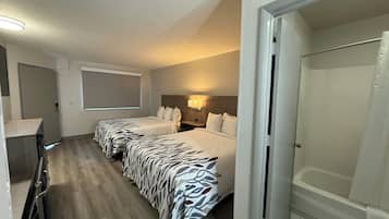 A hotel room with two beds, a shower, a desk, and a window.