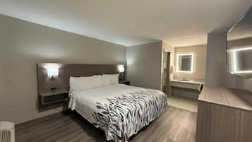 A hotel room with a bed, bedside lamps, a bathroom with a mirror and sink, and a wooden floor.