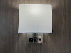 A wall-mounted light fixture with a textured shade and a control panel with three buttons. - Red Roof Reno (Reno)