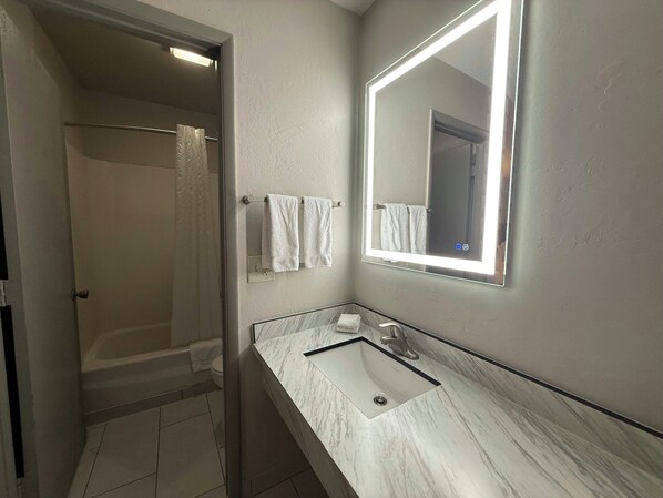 Une salle de bain avec une douche, un lavabo doté d’un plan de travail en marbre et un miroir avec éclairage.