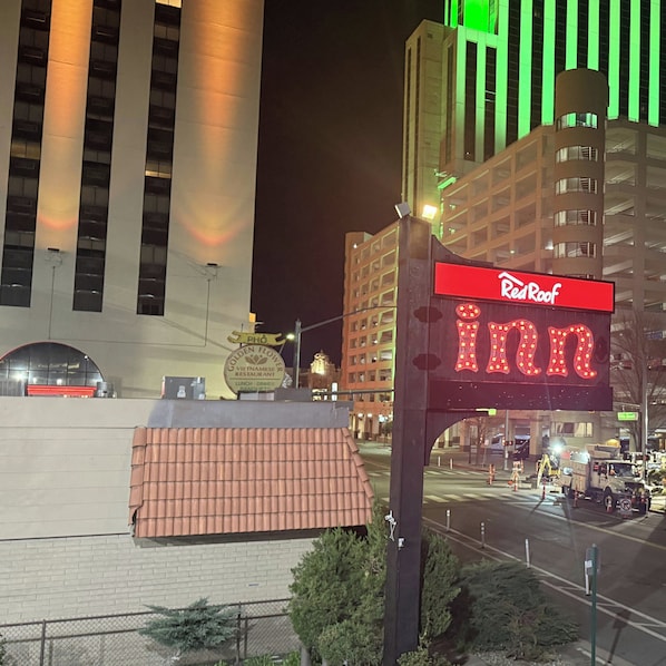 Segnaletica Red Roof Inn con una insegna luminosa al neon, un muro di mattoni e un edificio sullo sfondo con luci verdi verticali.