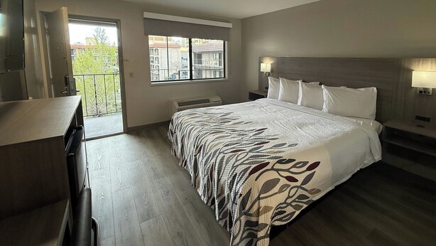 A bedroom with a large bed, a desk, a window, and a balcony. - Red Roof Reno (Reno)