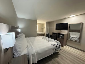 Une chambre d’hôtel avec un lit, un bureau, une télévision, un miroir et une salle de bain à l’arrière-plan.
