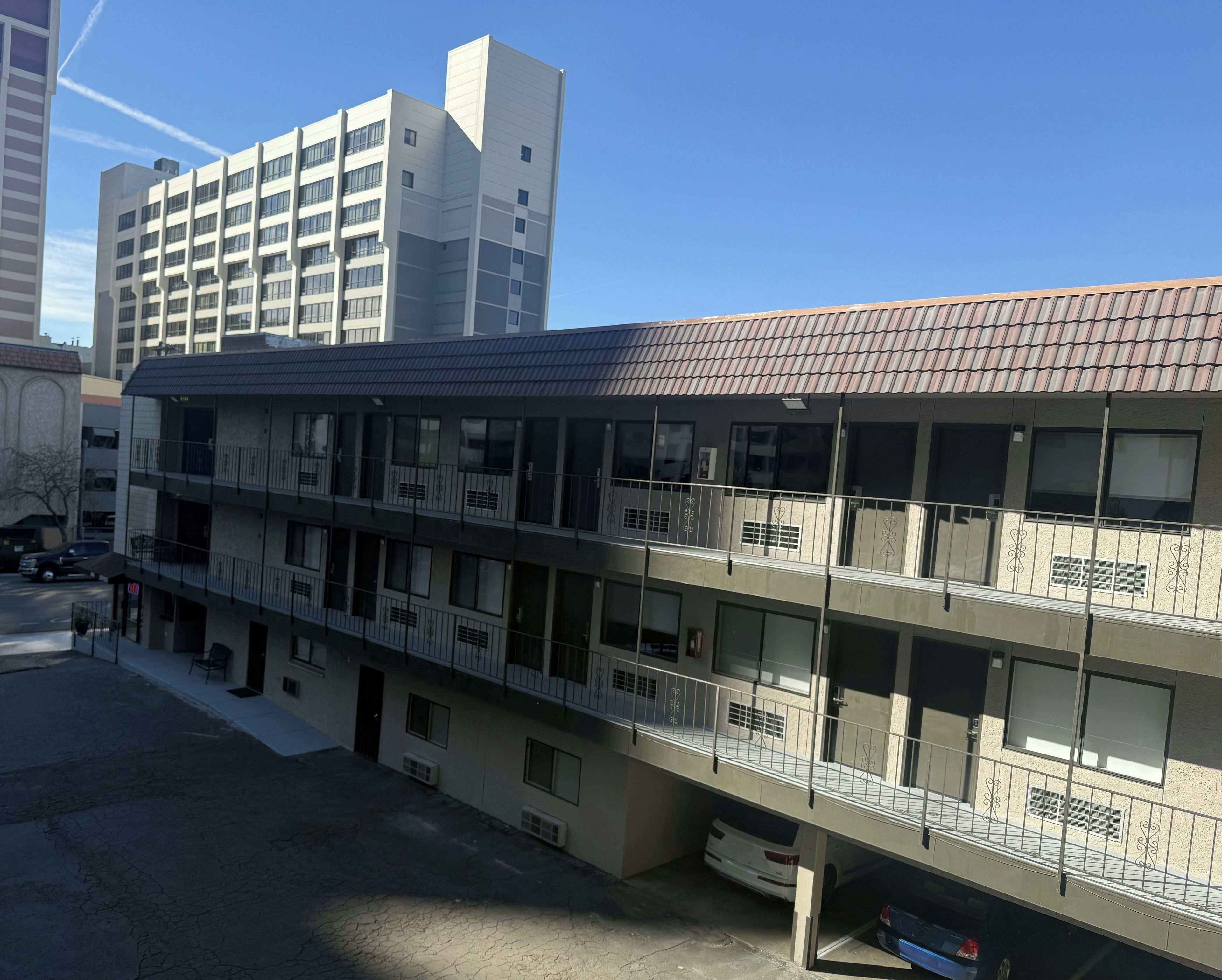 A multi-story building with balconies, a parking area, and a clear sky.