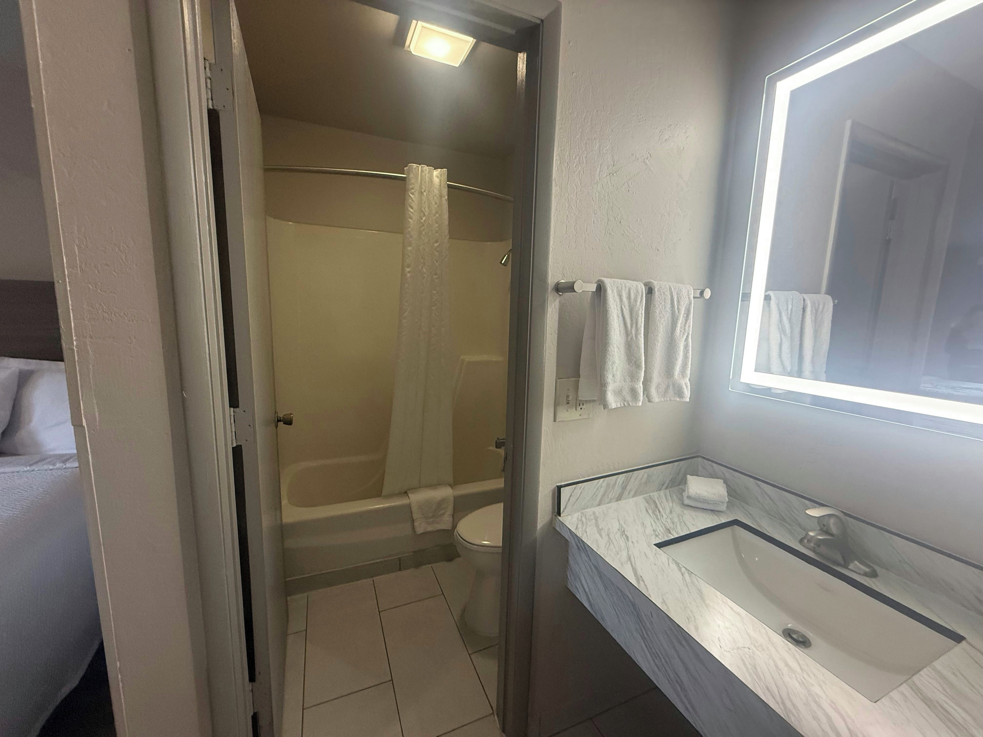 A bathroom with a glass shower enclosure, a marble sink, and a mirror with built-in lighting.
