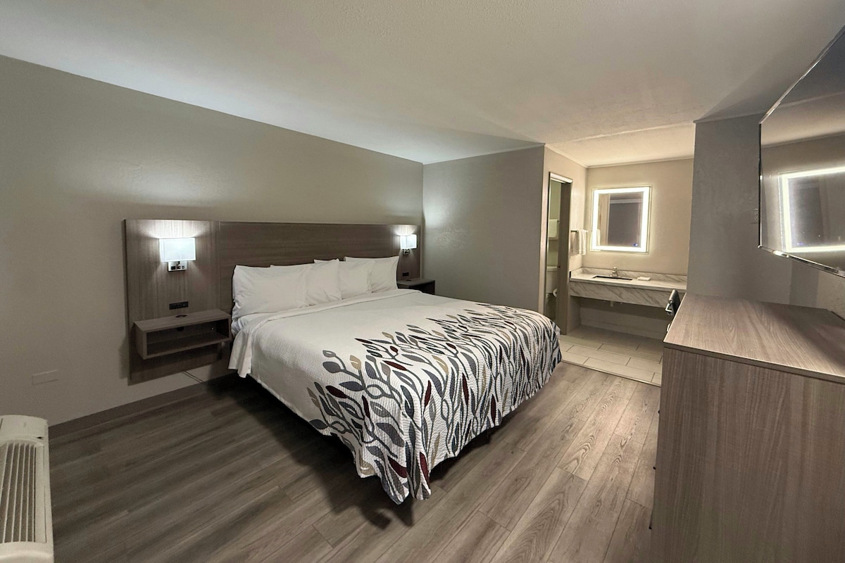 Une chambre d’hôtel avec un lit, des lampes de chevet, une salle de bain avec un miroir et un lavabo, et un plancher en bois.