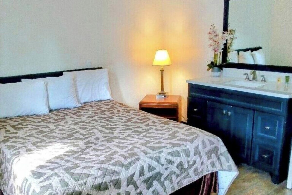 Habitació d'hotel amb un llit, una taula de nit, una làmpada i un mirall.