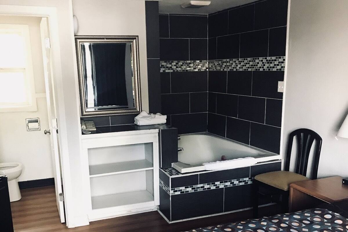 A hotel room with a bed, a small desk, a chair, a bathroom with a bathtub, and a mirror.