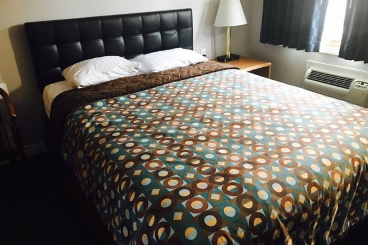 A hotel room with a bed, a nightstand, a lamp, and a window with curtains.