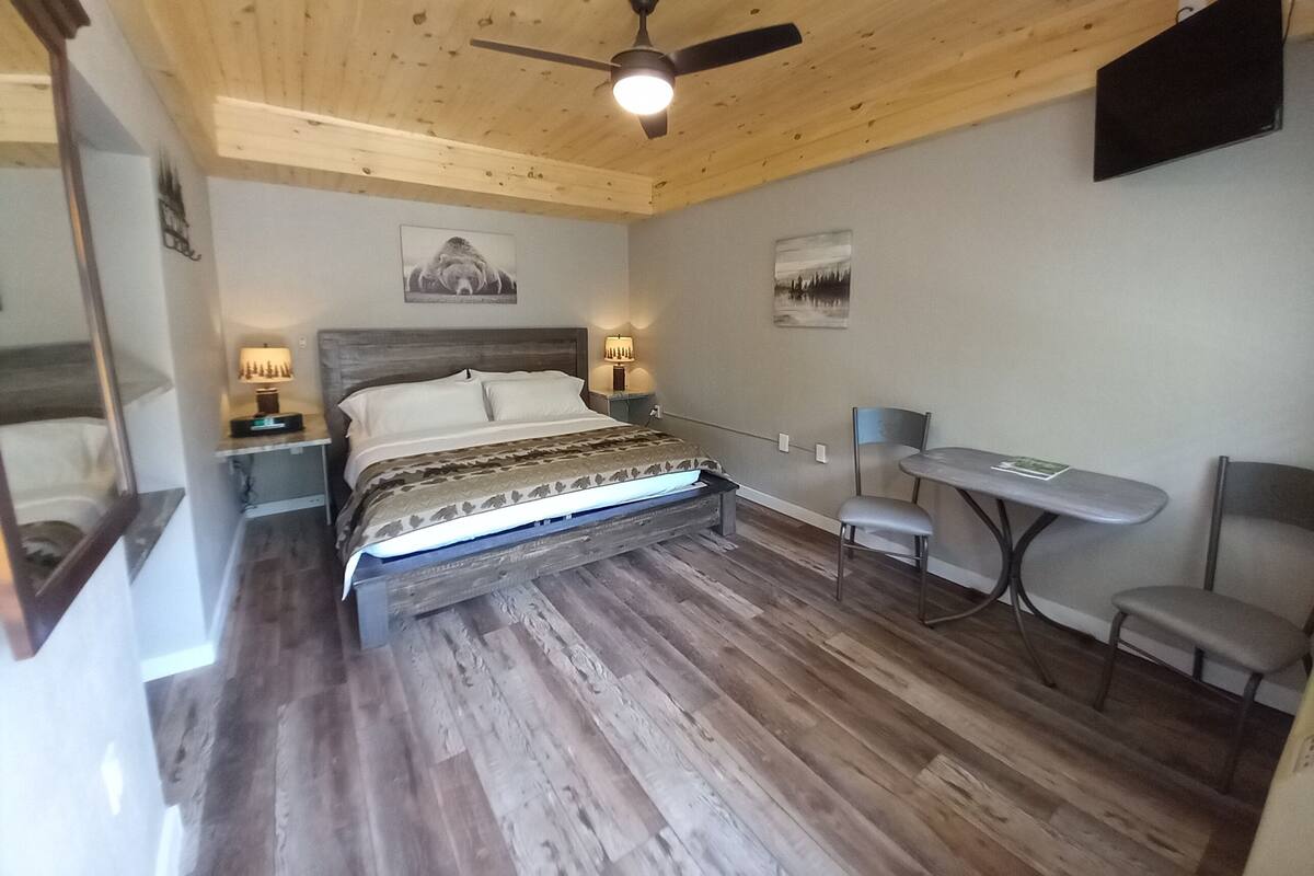 Ein Schlafzimmer mit Holzboden, einem Bett mit gemustertem Überwurf, einem Schreibtisch mit Stuhl und zwei Wandleuchten.