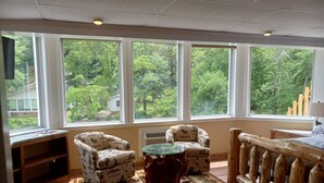 A room with large windows, a wooden bench, a table, and patterned armchairs. - The Carter Lodge On The River  (Chimney Rock)