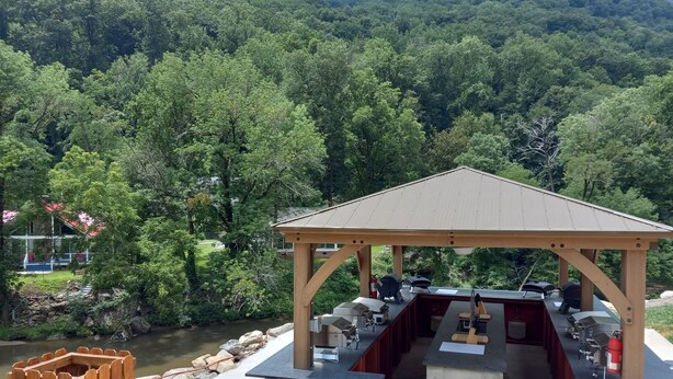 A covered outdoor area with a wooden structure, a concrete counter, and a view of a river and forested hills. - The Carter Lodge On The River  (Chimney Rock)