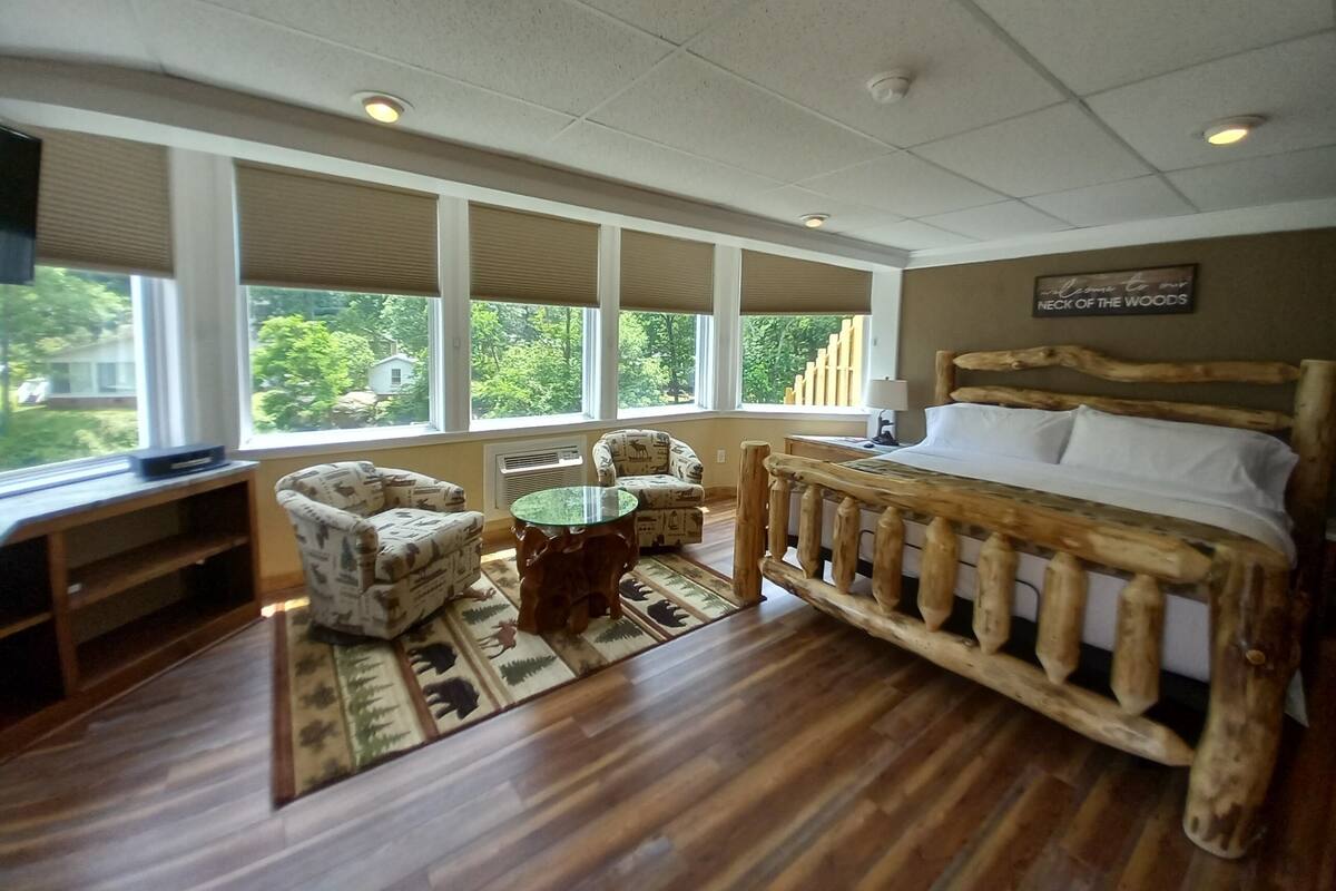 Ein Schlafzimmer mit einem hölzernen Bett, einem Fernseher, einer Couch und einem Fenster mit Blick auf Bäume.