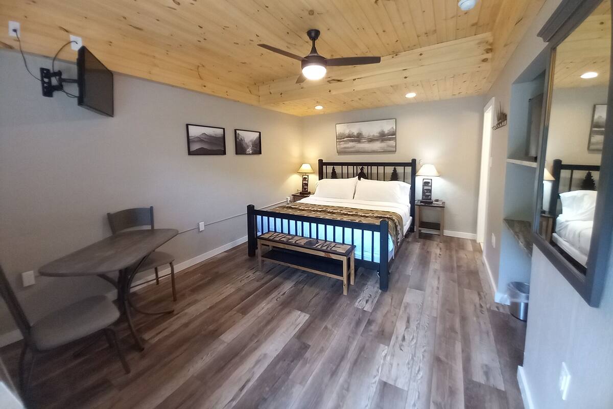 Ein Schlafzimmer mit Holzboden, einem Bett mit Kopfteil, Nachttischen mit Lampen, einem Schreibtisch mit Stuhl und einem Esstisch.