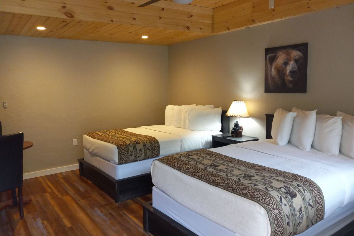 Ein Hotelzimmer mit zwei Betten, Holzböden, einem Deckenventilator, einer Lampe und einem Bärenbild an der Wand.