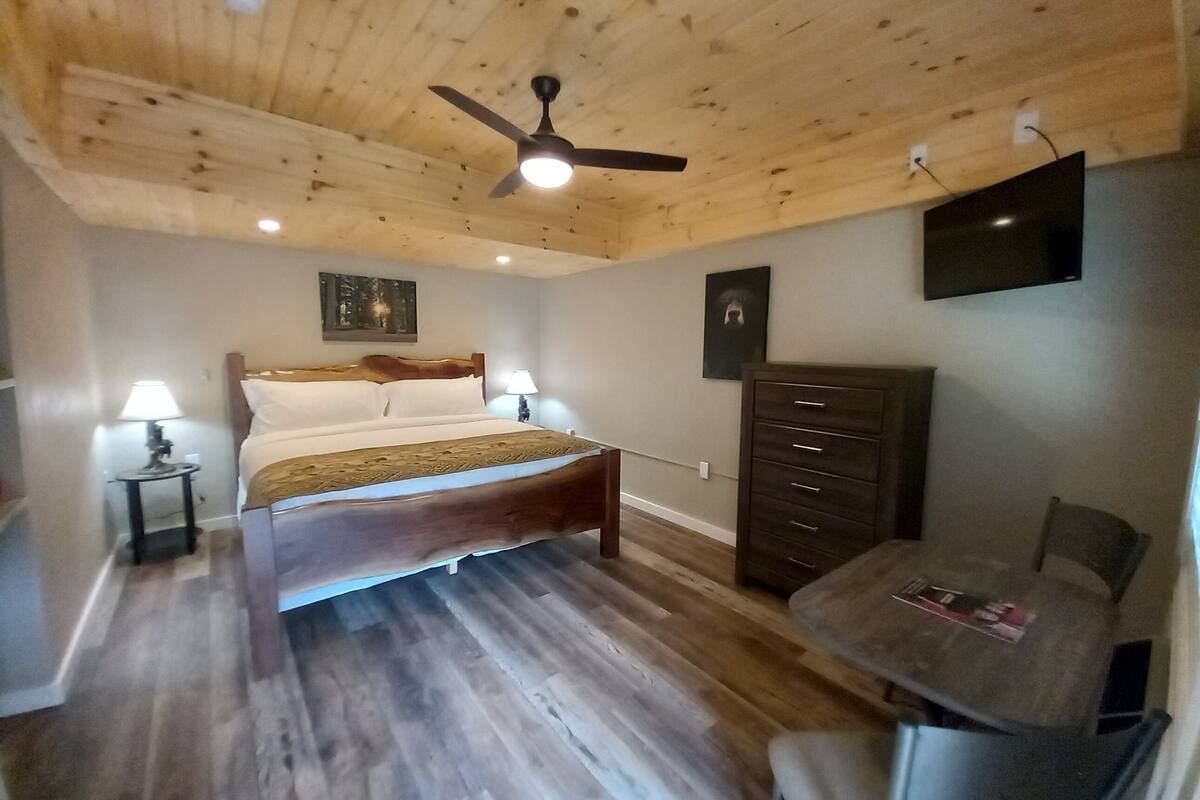Ein Schlafzimmer mit Holzboden, einem Bett, einem Schreibtisch, einem Sessel, einem Fernseher und einer Kommode.