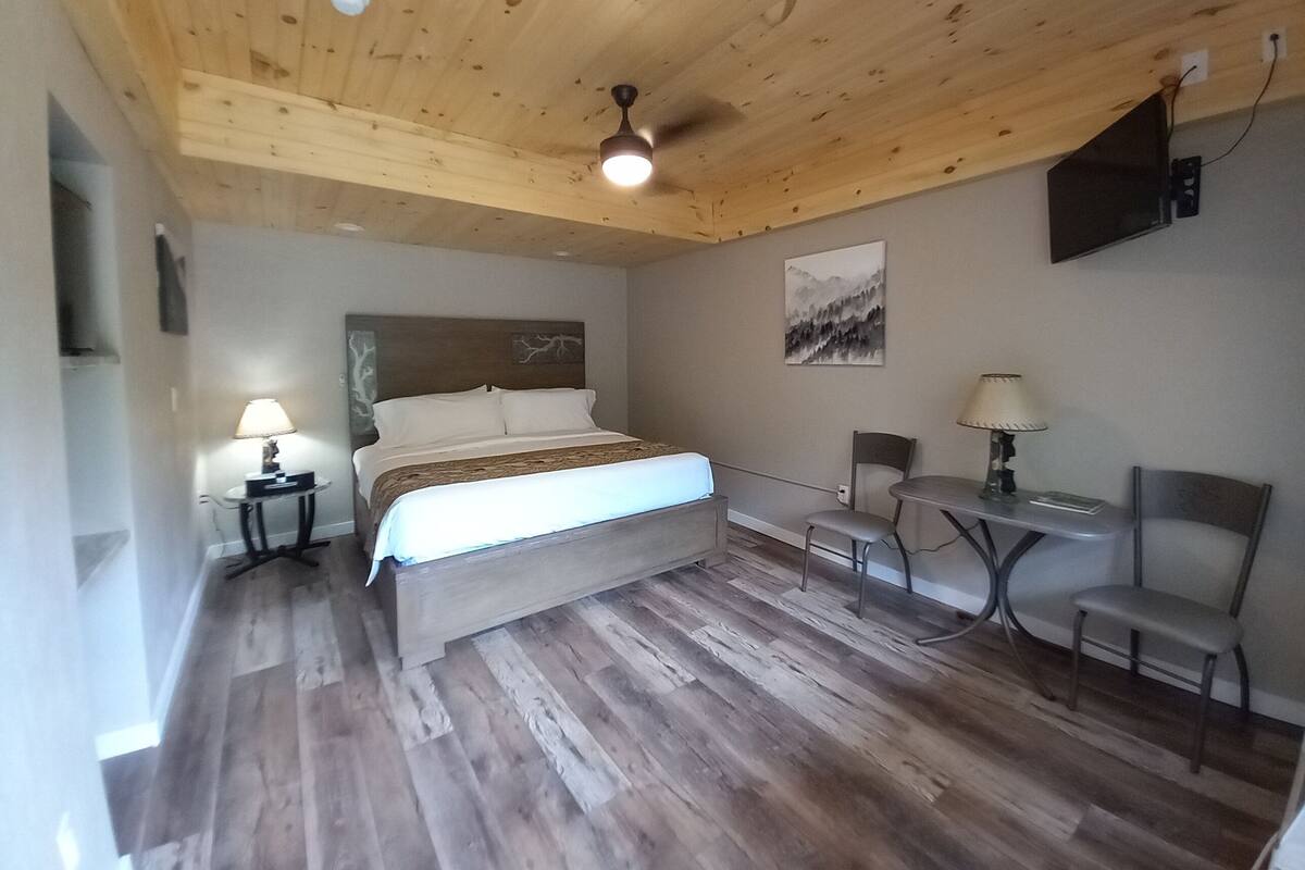 Ein Schlafzimmer mit Holzboden, einem Bett, einem Schreibtisch, zwei Stühlen und einer Lampe.