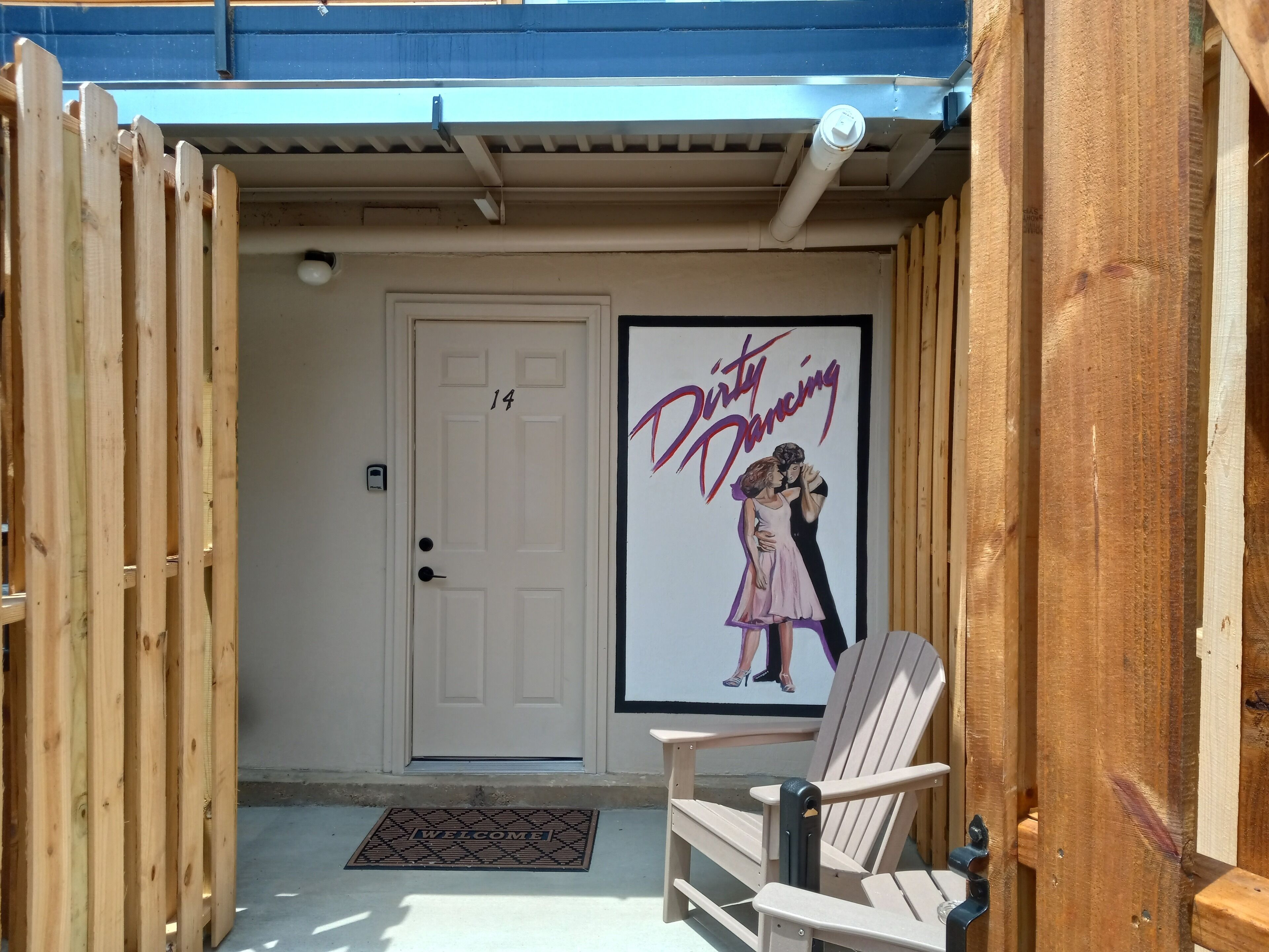 A wooden door with a number 14, a welcome mat, and a poster of 'Dirty Dancing' on the wall.