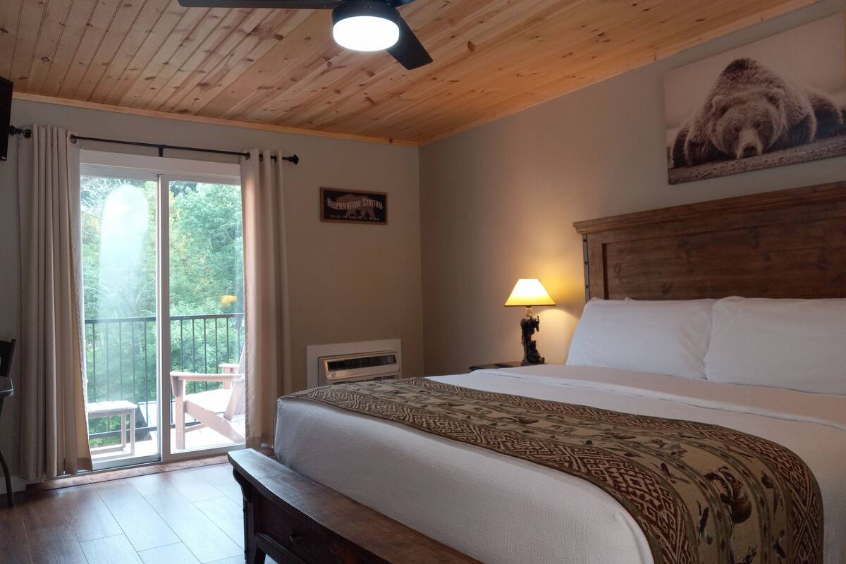 Ein Schlafzimmer mit einem Bett, einem Nachttisch, einer Lampe, einem Deckenventilator und einem Fenster mit Vorhängen.