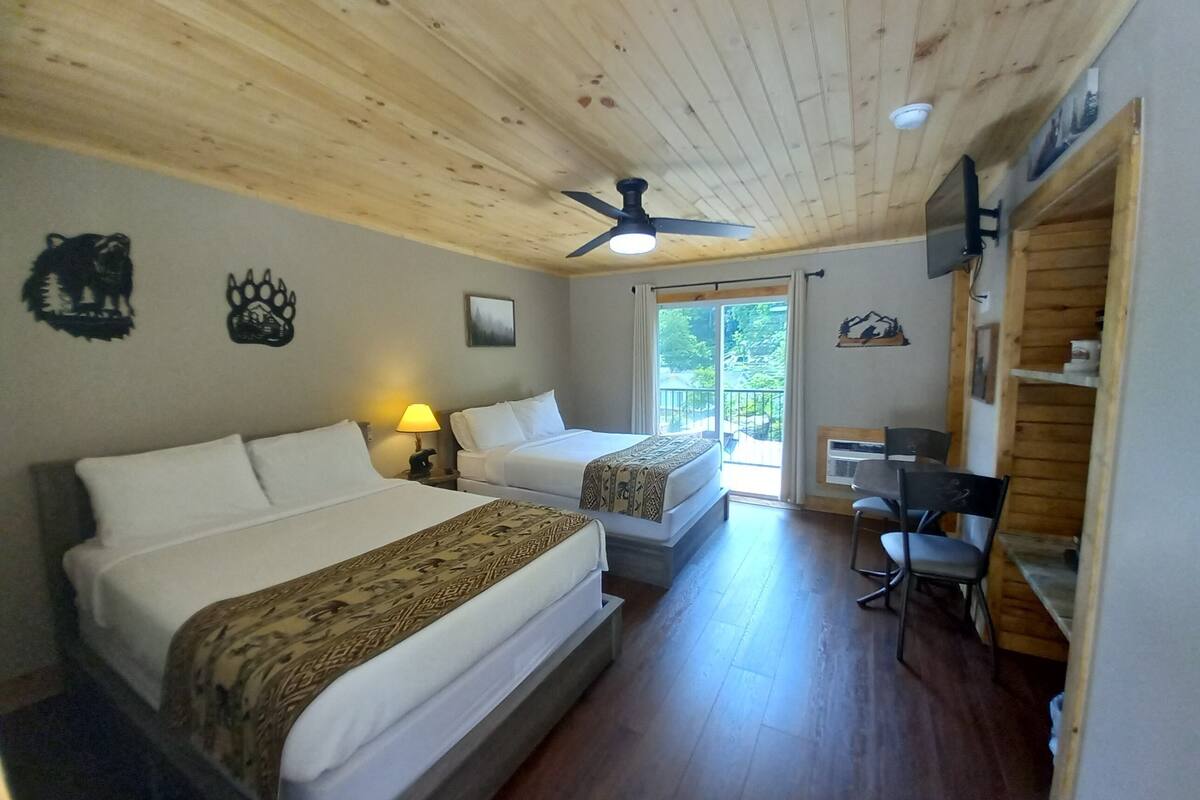 Ein Hotelzimmer mit zwei Betten, einem Schreibtisch, einem Sessel und einem Deckenventilator, mit Blick ins Freie.