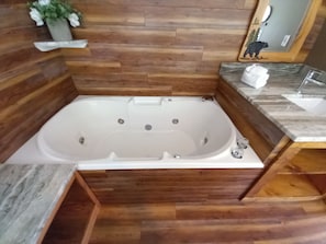 A bathroom with a wooden floor, a white bathtub, a marble countertop, and a mirror.