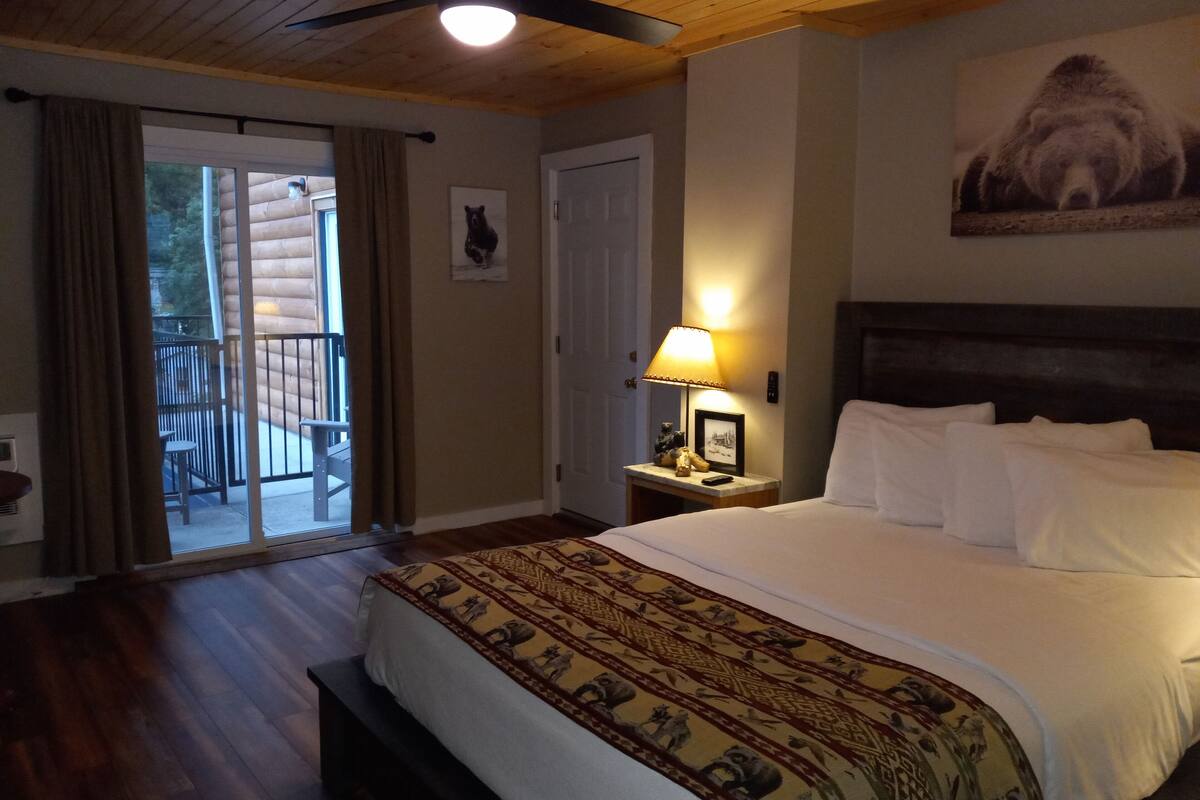Ein Schlafzimmer mit einem großen Bett, einem Nachttisch mit Lampe, einem Deckenventilator, einer Tür und einem Balkon mit Blick ins Freie.