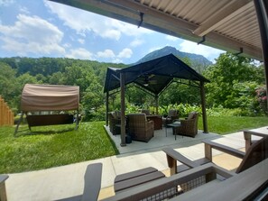 An outdoor patio with a covered seating area, a grill, and a view of a mountainous landscape.