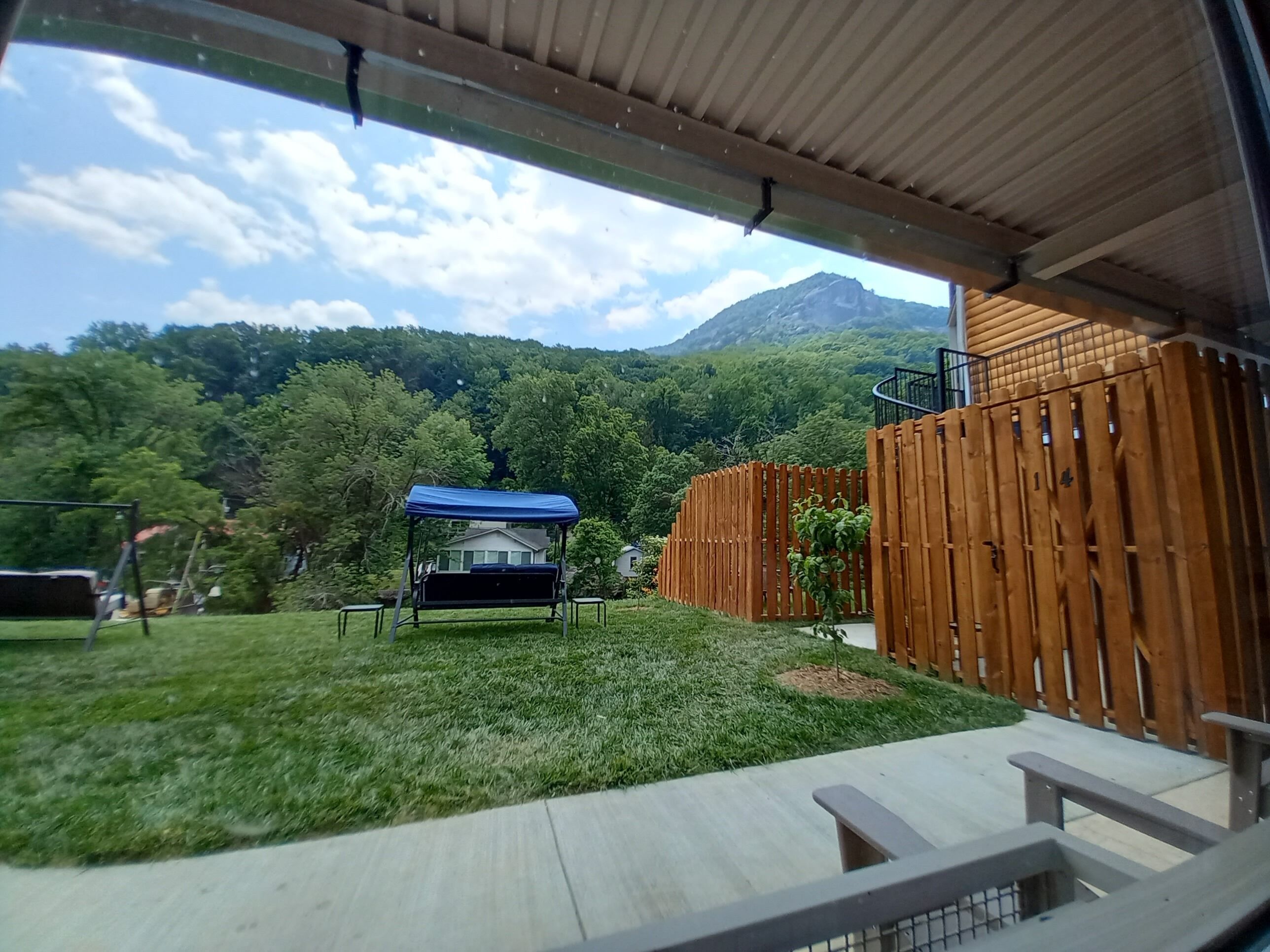 A covered patio area with a wooden fence, a swing set, and a small garden.