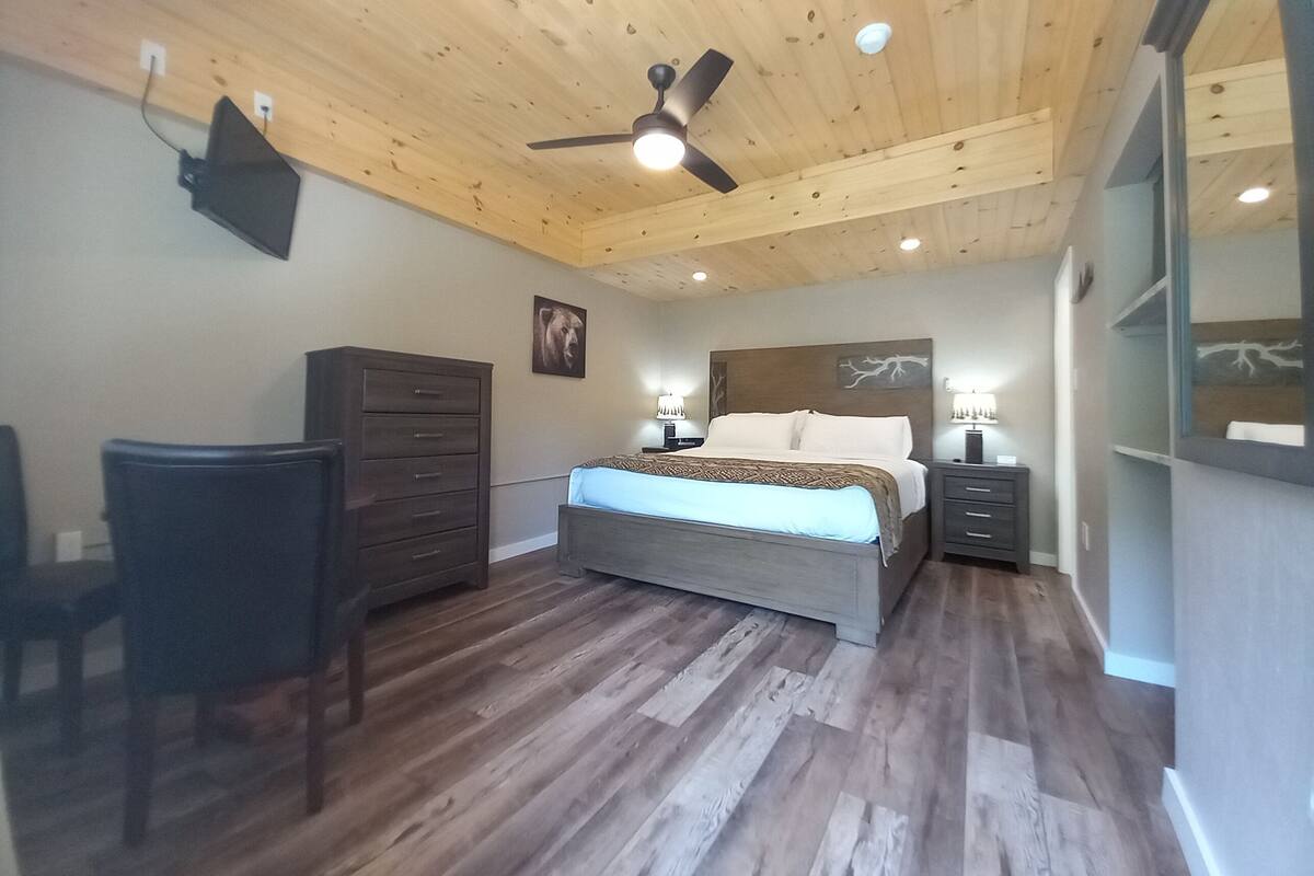 Ein Schlafzimmer mit Bett, Schreibtisch, Stuhl, Kommode und Deckenventilator.