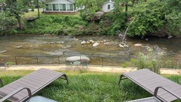 A riverside view with a grassy area and lounge chairs.