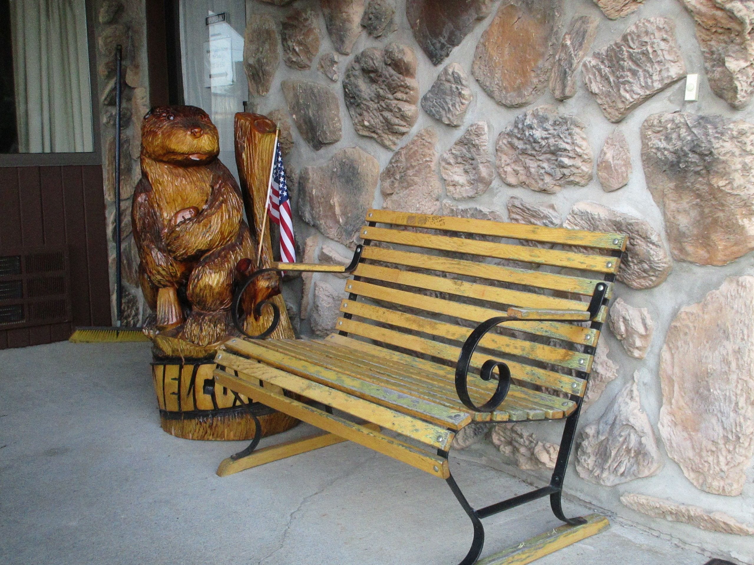 A wooden bench with a bear sculpture and an American flag.