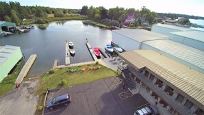 En småbåtshamn med förtöjda båtar, en gräsyta med utomhusmöbler och en stor industribyggnad.